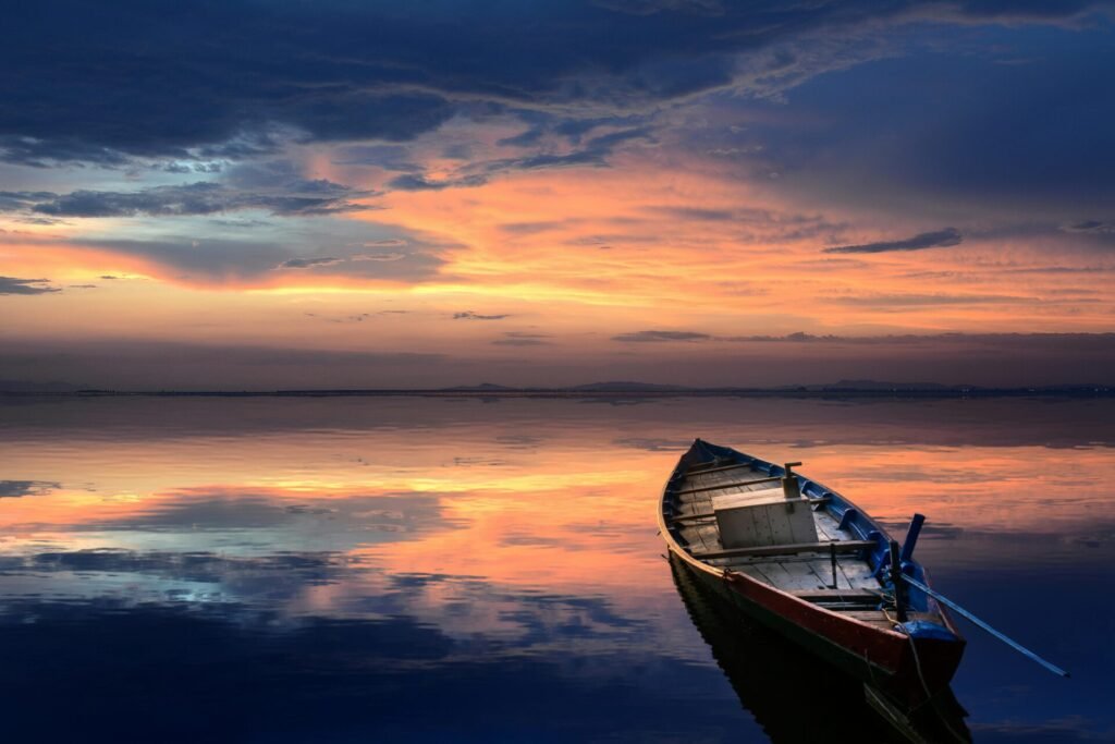 A serene scene of a wooden boat floating on a calm sea at sunset, reflecting vibrant colors and a tranquil atmosphere.